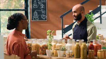 Vendor presents bulk products in jars, recommending type of bio organic pasta to female customer in local grocery store. Young man showing bulk products in recyclable containers, healthy eating. photo