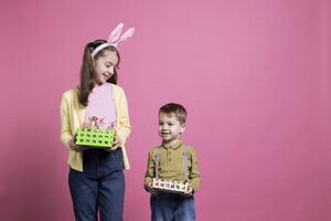 Cheerful young girl and boy posing with their festive baskets, decorated and painted eggs for easter celebration in studio. Adorable siblings showing handmade spring arrangements. photo