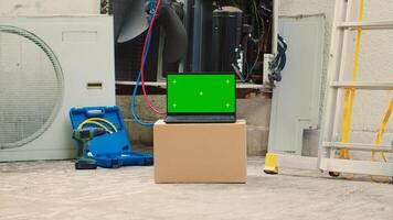 Green screen laptop in front of out of service outside air conditioner. Mock up chroma key gadget display next to damaged external HVAC system in need of expert maintenance photo