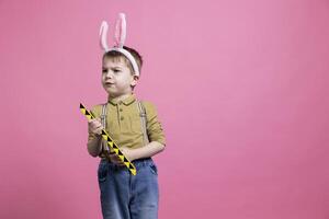 Upset little toddler playing with a toy and being displeased about something, wearing a pair of bunny ears for easter celebration. Young child feeling irritated and sad, adorable innocent kid. photo