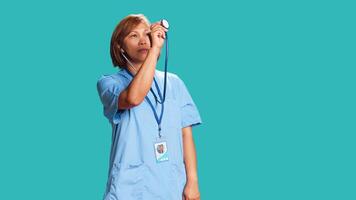 Experienced asian healthcare specialist using stethoscope, measuring vital signs. Nurse isolated over studio background utilizing professional medical device to provide diagnostic photo