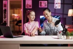 Excited child and her mom do content creation using professional recording equipment to film vlog channel intro. Daughter and parent greet fanbase, presenting today video topic in pink neon studio photo