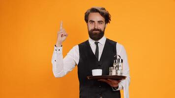 Elegant butler having new idea on camera, raising index finger and indicating upwards direction with restaurant food tray in hand. Skilled waiter feeling genious, innovative with fresh thoughts. photo