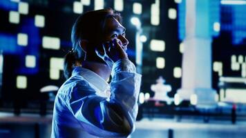 Smiling man talking over the phone with girlfriend using smartphone to feel less bored while strolling around dimly illuminated empty avenues at night, blurry urban landscape background photo