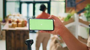 Seller showing greenscreen on phone display, presenting isolated mockup template on gadget in local organic zero waste store. Young man vendor using blank chromakey copyspace screen. photo