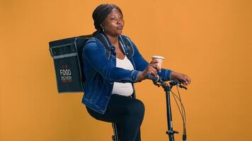 africano americano mujer en bicicleta disfrutando taza de café antes de trabajando su acelerado entrega Servicio trabajo. juvenil hembra mensajero relajante después Bajo demanda paquete entregas foto