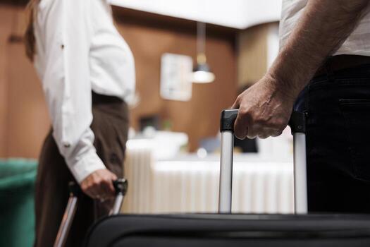 Close view of couple entering foyer of fancy hotel with trolley bags. Detailed shot of elderly individuals grasping suitcases as they walk up to registration desk to check in with the receptionists. photo