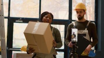 Warehouse employees using smartphone placed on tripod to make video for social media promoting the company. Coworkers filming themselves in storage room showcasing their daily tasks photo