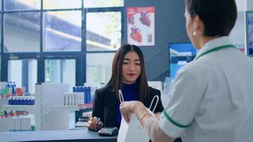 Asian woman in drugstore at checkout counter using credit card to purchase medical items. Happy customer doing contactless paying in pharmacy after finding needed virus stopping pills photo