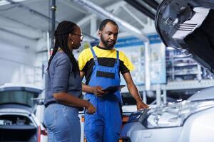 Mechanic at auto repair shop conducts annual vehicle checkup, informing customer about needed exhaust system replacement. Certified garage worker talks with customer after finishing car inspection photo