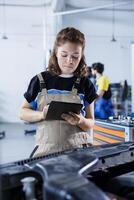 Technician in car service uses tablet to calculate invoice for client after repairing lights system. Skilled garage employee calculating final costs after servicing customer vehicle photo