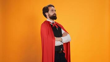 Powerful comic superhero with red cape standing against yellow background, feeling strong on camera. Dedicated valet superhuman with mantle working in restaurant dining industry. photo