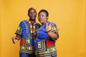 Man and woman couple dancing and singing together while looking at camera. Mid adult african american wife and husband pair making moves and talking while posing for portrait photo