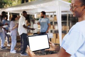 Image shows friendly african american lady carrying tablet with copyspace mockup template for customizable charity notes. Smiling woman horizontally grasps digital device with isolated white screen. photo