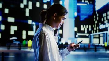Man walking around city buildings at night, scrolling on ecommerce website, looking at clothes, blurry cityscape background. Person using smartphone while strolling on empty streets photo