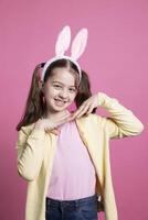 Cute schoolgirl with pigtails and bunny ears fooling around in the studio, playing and doing dance moves. Positive cheerful kid feeling confident and excited about easter, beautiful toddler. photo
