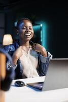 Black woman smiling wide and happily while using a digital personal computer in her apartment. Excited african american blogger seated in front of laptop, having a video conference call. photo