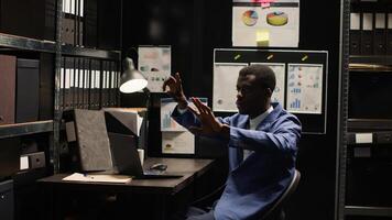 Black policeman investigates complex case, surrounded by evidence, files, and holographic displays. Private detective using artificial intelligence to examine evidence on hologram in incident room. photo