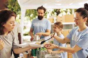 At an outdoor food bank, caucasian family volunteering a variety of food items to assist the hungry and less fortunate individuals. Nonprofit group supports hunger relief by serving nutritious meals. photo