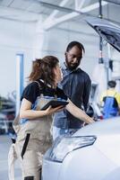 Mechanic in car service ordering new ignition system for damaged vehicle using tablet. Employee next to BIPOC client looking online for components to replace old ones in malfunctioning automobile photo