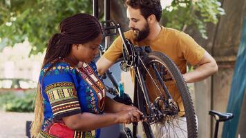 Multiethnic couple working together to repair and maintain damaged bike for summer cycling. Caucasian boyfriend helps girlfriend in choosing suitable tool for fixing bicycle hub and axle in yard. photo