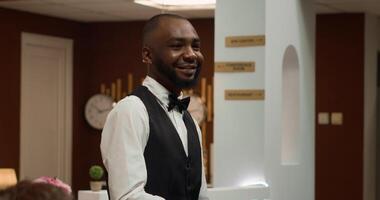 Hotel concierge offering services to guest and help with trolley bags, providing excellent assistance in lounge area lobby. African american front desk staff carrying luggage. Handheld shot. photo