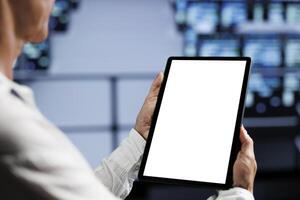Close up shot of mock up tablet used by licensed IT expert in data center using server rows to deliver massive computing power, control network resources, process and store datasets photo
