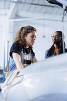 Hardworking mechanic at auto repair shop conducts annual vehicle checkup, informing client about needed engine replacement. Garage expert talks with customer after finishing car inspection photo