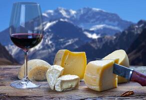 Table with a glass of red wine and various cheeses photo