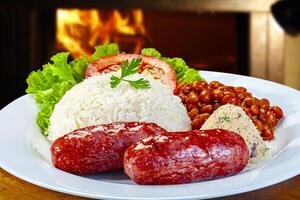 Plate with sausage, rice, beans, salad and farofa photo