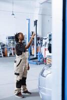 Trained mechanic in repair shop using holographic augmented reality to visualize car parts in order to fix them. BIPOC woman using AR technology while working on defective vehicle battery photo