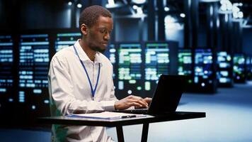 African american serviceman evaluating mainframes helping enterprises manage databases and store files. Professional inspecting server farm electronics used for high performance computing photo