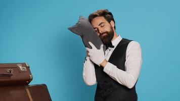 soñoliento botones posando con almohada en estudio, publicidad agotamiento y siendo sobrecargado de trabajo en de buen tono hospital industria. hotel portero tomando rápido siesta después trabajando con el tiempo, cansado portero. foto