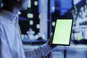 Person having fun walking around city at night, scrolling on online shopping platform using mockup tablet, close up. Citizen using chroma key device while strolling in empty urban environment photo