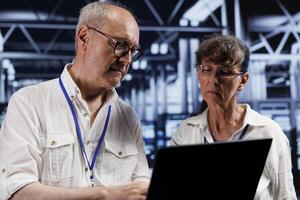 Octogenarian engineers doing diagnostic assessments on servers to detect problems with high tech facility electronics. Technicians during routine maintenance looking for potential system difficulties photo