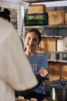 Portrait of smiling young female giving free food to someone in need at an outdoor food bank. Close-up of a girl happily providing hunger relief and support to the poor and homeless people. photo