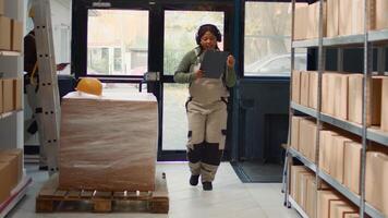 Happy warehouse sorter listening music enjoying herself while checking labels on cardboard boxes. Cheerful worker wearing heaphones and dancing around while walking through storage room rows photo