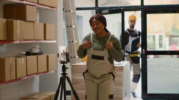 Warehouse employee using cellphone placed on tripod to do training video for interns and coworker arriving at work greeting them. Worker showing trainees how to effectively arrange goods photo