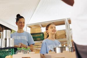 Caucasian mother and daughter volunteering at food drive, providing free food to the poor and needy. Female charity workers helping and giving essential items to homeless people and less fortunate. photo