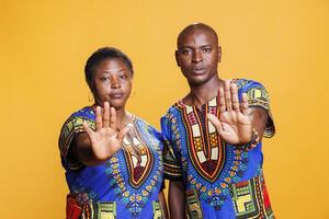 Confident man and woman showing stop gesture with palms studio portrait. African american couple showcasing refuse signal and looking at camera with serious face expression photo