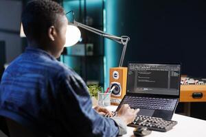 Focused African American woman managing software and programming code on laptop. Skilled female programmer with wireless computer, providing online services and maintaining network security. photo