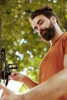 comprometido sano y energético hombre ajustando y asegurando bicicleta partes para agradable verano ciclismo. joven masculino caucásico ciclista reparando bicicleta rueda como anual mantenimiento al aire libre. foto