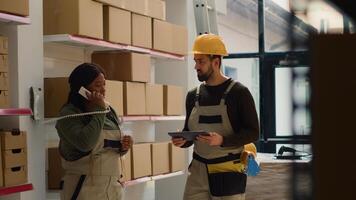 Production technician and warehouse picker preparing orders for delivery, receiving phone call with updated instructions in retail stockroom while scanning labels on parcels to be shipped photo