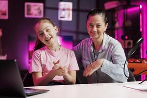 Young girl and her mom using professional gear to shoot intro for family vlog channel on online platforms. Cheerful daughter and parent warmly welcoming dedicated gen Z fans, filming in home studio photo