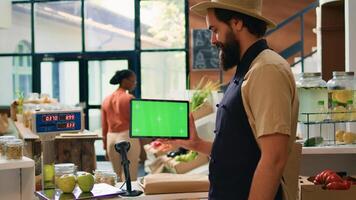 Storekeeper holds tablet with greenscreen in zero waste eco supermarket, using copyspace mockup on mobile gadget standing at checkout counter. Small business owner presents isolated display. photo