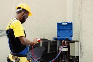 Proficient african american worker doing routine condenser maintenance, assembling manifold indicators before starting work. Qualified electrician getting equipment ready to check freon leaks photo