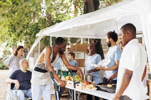 Caring charity workers serve warm meals to the less privileged outdoors, aiding both wheelchair users and those on crutches. Humanitarian aid team supporting the poor, disabled and homeless people. photo