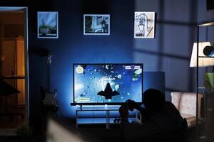 Player participates in online roleplaying firing match, hooking console through TV and enjoying nighttime gaming activity with friends. Male student is playing shooter video games. photo