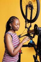 deportivo africano americano hembra ciclista reparando y mantener a garantizar de primera categoría actuación. detallado ver de sano negro mujer meticulosamente examinando y de corrección bicicleta pedal. foto