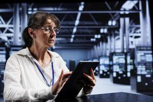 Old computer scientist using tablet to assess server cybersecurity problems arising due to unsecured network connections. Adept worker ensuring high tech location is impenetrable by ddos attacks photo